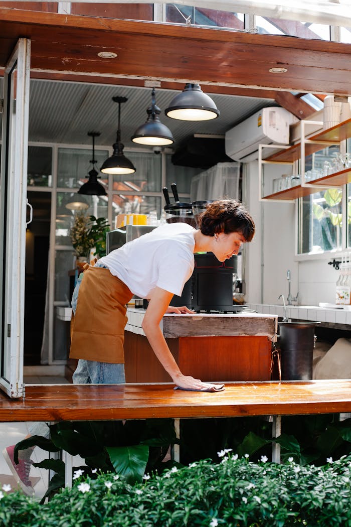 gallery-05 A barista wiping down a café counter, showcasing cleanliness and professionalism in a bright, airy setting.